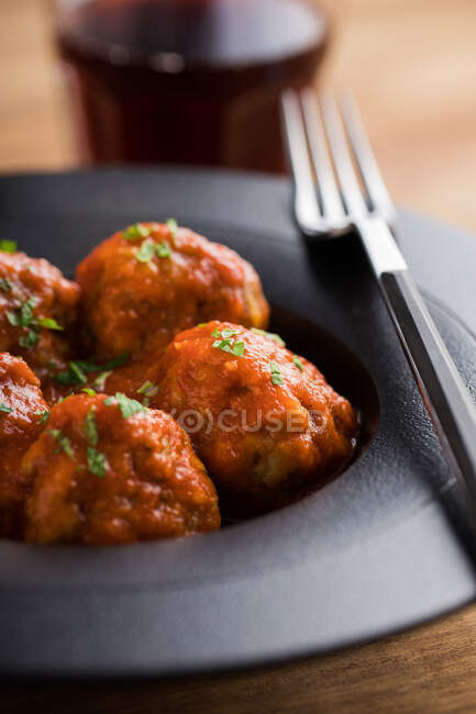 De arriba sabrosas albóndigas cocidas con salsa de tomate que sirven con pan en plato negro con cubiertos y bebidas en la mesa - foto de stock