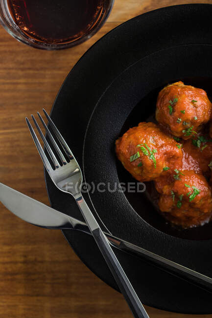 From above tasty cooked meatballs with tomato sauce serving with bread on black plate with cutlery and beverage on table — Stock Photo