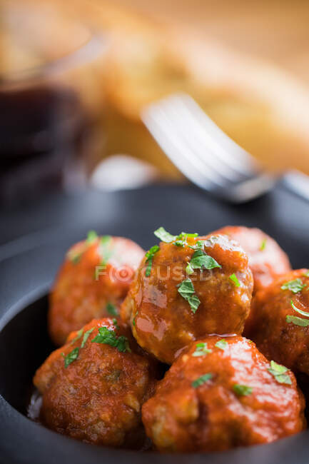 Dall'alto gustose polpette cotte con sugo di pomodoro che servono con pane su piatto nero con posate e bevande in tavola — Foto stock