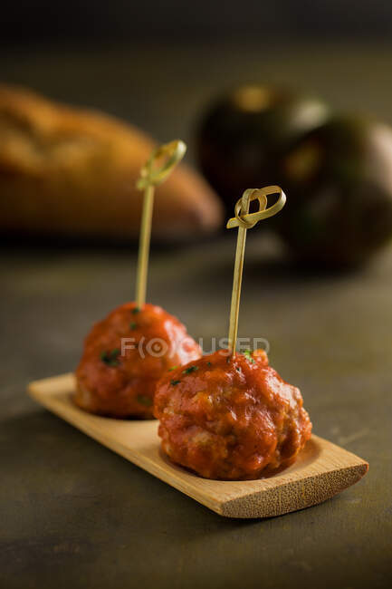 Вкусные мясные шарики с томатным соусом, прикрепленные бамбуковыми палочками на плоской доске на столе — стоковое фото