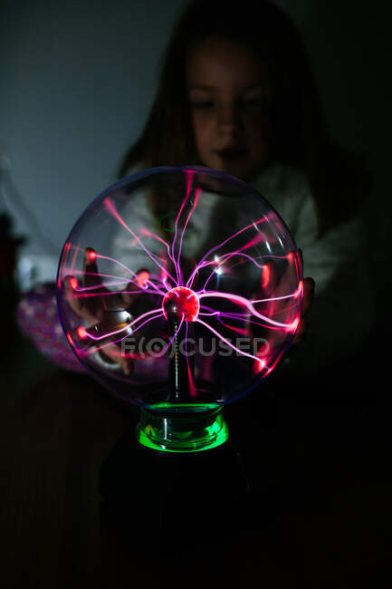 Charmed girl touches glowing ball with hand in dark — Stock Photo