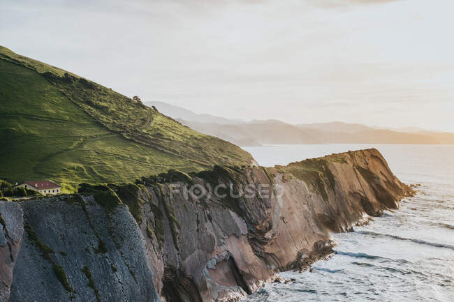 Small cottages in green rocky valley on shore washing by ocean in bright day — Stock Photo