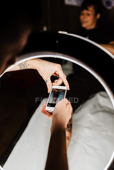 Tatuaggio uomo irriconoscibile utilizzando lo smartphone per scattare foto del tatuaggio sulla gamba del cliente del raccolto per portafoglio in studio contemporaneo — Foto stock