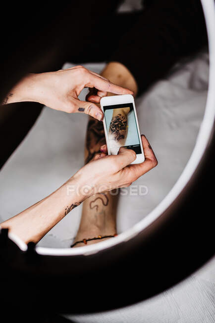 Unrecognizable man tattooer using smartphone to take picture of tattoo on leg of crop customer for portfolio in contemporary studio — Stock Photo