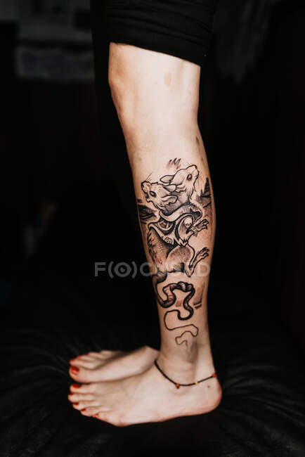 Unrecognizable female with pedicure and stylish two headed rat tattoo on leg standing in dark salon — Stock Photo