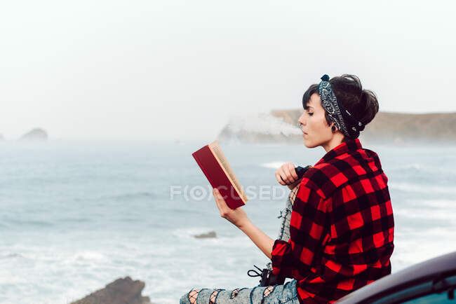 Задумчивая женщина с книгой на берегу моря — стоковое фото