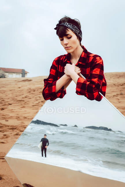Sad woman with big mirror standing on beach — Stock Photo
