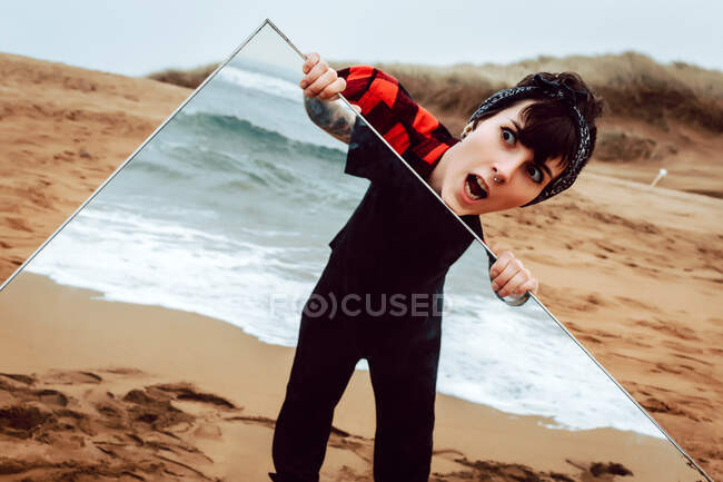 Donna sulla spiaggia tenendo specchio con riflesso maschile — Foto stock