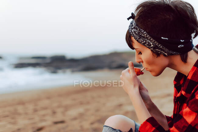 Frau zündet sich Zigarette am Strand an — Stockfoto
