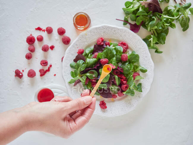 From above crop cook adding juice with spoon to tasty fresh salad with ripe raspberries and fresh spinach — Stock Photo