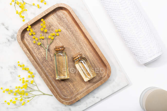De cima vista superior da flor de mimosa e seu óleo essencial na bandeja de madeira na mesa de fundo de mármore — Fotografia de Stock
