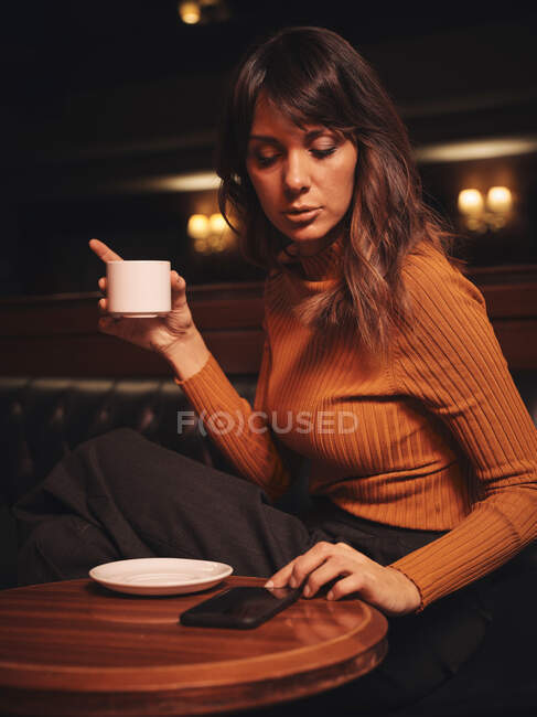 Mulher inteligente surfar celular confortavelmente sentado na mesa redonda e surfar telefone celular — Fotografia de Stock
