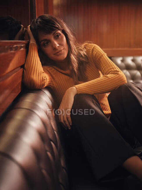 Романтичная очаровательная женщина мечтает комфортно сидеть на черном кожаном диване — стоковое фото