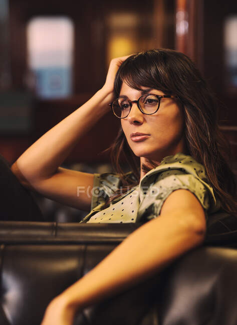 Вид збоку втомленої розслабленої жінки, що спирається на шкіряний чорний диван і дивиться в кафе — стокове фото
