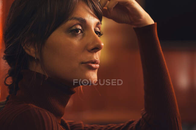 Mulher elegante na moda em roupas da moda sentado no sofá de couro preto e olhando para longe — Fotografia de Stock