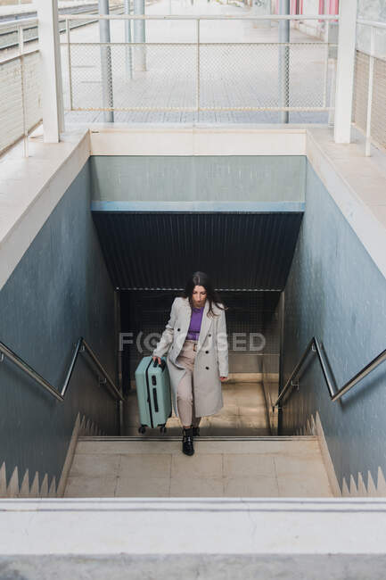De cima de elegante jovem viajante elegante com mala subindo escadas na estação de trem — Fotografia de Stock