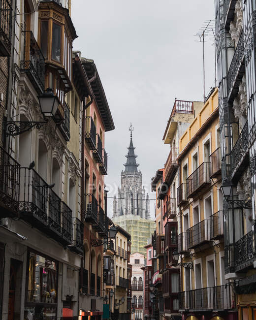 En dessous de la rue étroite de la ville Tolède en Espagne avec de vieux bâtiments résidentiels et cathédrale en arrière-plan contre un ciel gris nuageux — Photo de stock