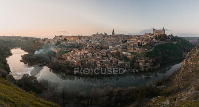 Панорамний вид через річку старого міста Толедо в Іспанії з середньовічними замками і фортецями в час заходу сонця з хмарним небом і відображенням у річковій воді. — стокове фото