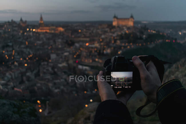 Schnitthände eines männlichen Fotografen mit Kamera, die auf einem Hügel steht und die alte spanische Stadt Toledo mit Schlössern in der Dämmerung fotografiert — Stockfoto