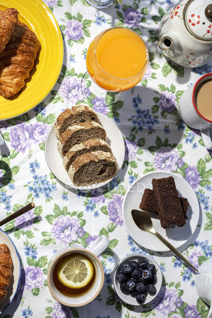 De cima vista superior de pequeno-almoço caseiro completo sob luz solar com ovos cozidos, mirtilos, bolo de esponja, croissants, torradas, chá, café e suco de laranja — Fotografia de Stock