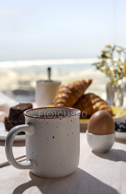 Pequeno-almoço caseiro completo sob luz solar com ovos cozidos, mirtilos, bolo de esponja, croissants, torradas, chá, café e suco de laranja — Fotografia de Stock