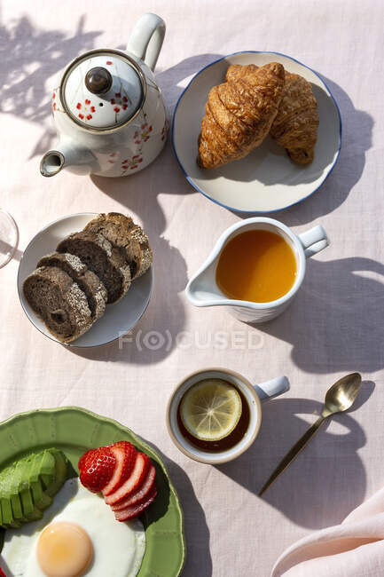 Petit déjeuner complet sain fait maison au soleil avec œufs, avocat, fraises, bleuets, gâteau éponge, croissants, pain grillé, thé, café et jus d'orange — Photo de stock