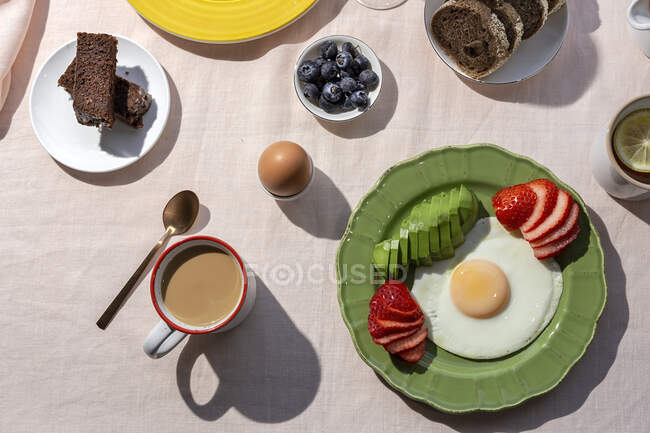 Colazione sana e completa fatta in casa alla luce del sole con uova, avocado, fragole, mirtilli, pan di Spagna, croissant, toast, tè, caffè e succo d'arancia — Foto stock