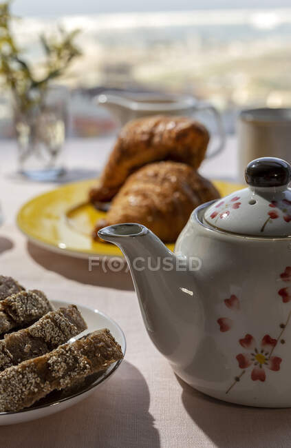 Hausgemachtes komplettes Brunch-Frühstück im Sonnenlicht mit Tee oder Kaffeekanne, Brotscheiben und Croissants — Stockfoto