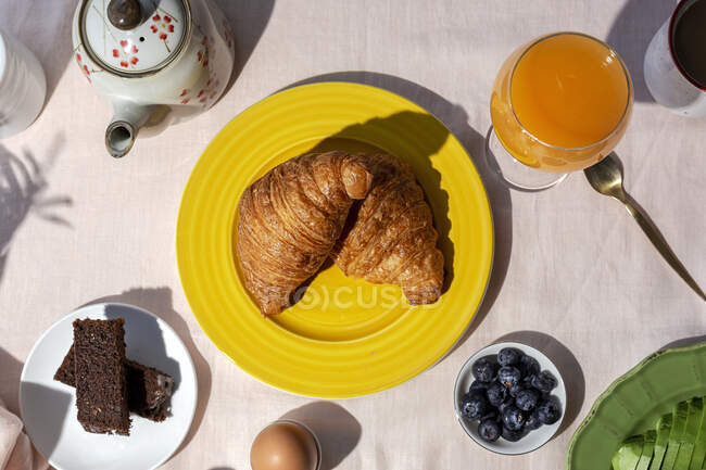 Сверху вид на домашний завтрак с полным завтраком в солнечном свете с круассанами, клубникой, чаем или кофе и апельсиновым соком — стоковое фото