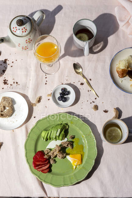 Pequeno-almoço caseiro e saudável à luz do sol com ovos, abacate, morangos, mirtilos, bolo de esponja, croissants, torradas, chá, café e suco de laranja — Fotografia de Stock