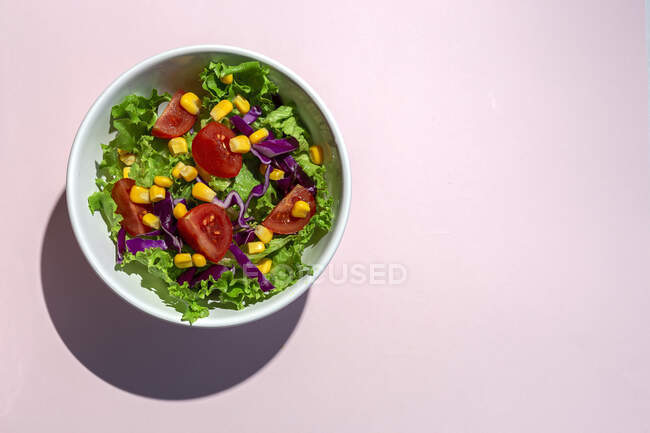 Frischer Salat mit Kirschtomaten, roten Zwiebeln und Mais, Sonnenlicht auf rosa Hintergrund von oben. Gesunde Ernährung. Veganes Essen. — Stockfoto