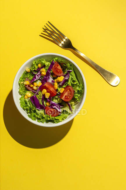 Frischer Salat mit Kirschtomaten, roten Zwiebeln und Mais, Sonnenlicht auf rosa Hintergrund von oben. Gesunde Ernährung. Veganes Essen. — Stockfoto
