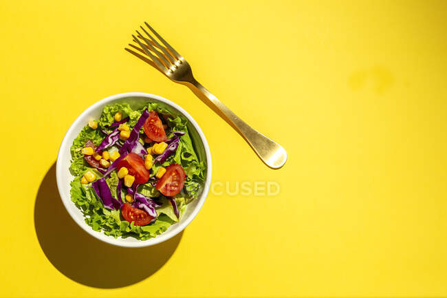 Salade de laitue fraîche avec tomates cerises, oignon rouge et maïs, lumière du soleil sur fond rose d'en haut. Une nourriture saine. Alimentation végétalienne . — Photo de stock