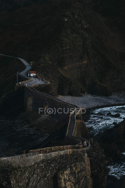 Die kurvenreiche Bergstraße überquert eine Steinbrücke und führt in der Dämmerung an der felsigen Küste Spaniens entlang — Stockfoto
