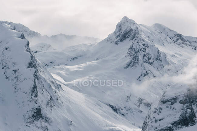 Grave freddo paesaggio invernale con cime rocciose innevate e luce del sole che irrompe nella nebbia e nella tempesta di neve — Foto stock