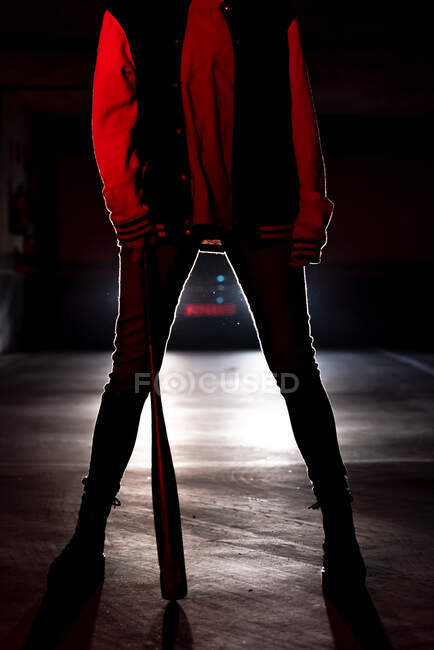 Pernas de corte de mulher sem rosto em jeans e botas pretas com bastão maciço único segurando com faróis de carro no fundo — Fotografia de Stock