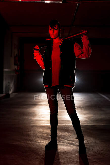 Young hipster woman in jeans and black boots with massive sole holding bat with car headlights on background — Stock Photo