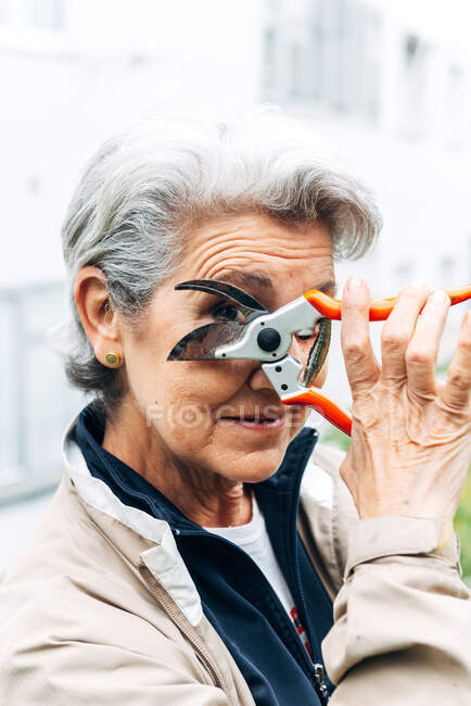 Satisfied mature female gardener looking at camera through garden equipment in garden — Stock Photo