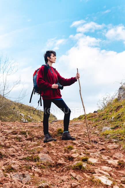 Турист с рюкзаком и палкой смотрит в сторону во время похода на холм под облачным небом в Испании — стоковое фото
