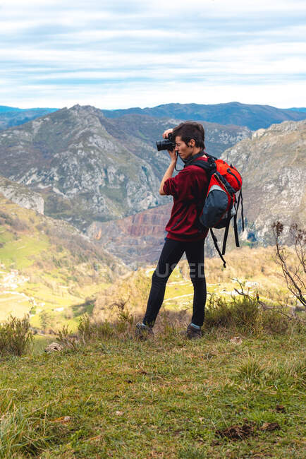 Seitenansicht einer Frau mit Rucksack, die auf einer Waldlichtung steht und mit der Kamera ein herrliches Tal vor nebligen Bergrücken am Horizont unter wolkenverhangenem Himmel in Spanien fotografiert — Stockfoto
