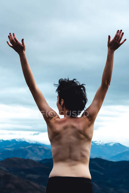 Vue arrière de la femelle libre topless debout avec les bras levés jouissant de la liberté et de la sauvagerie tout en regardant des paysages idylliques de montagne brumeuse par temps couvert en Espagne — Photo de stock