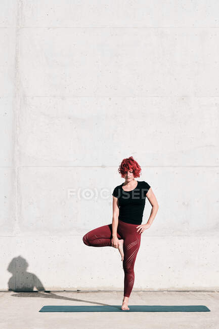 Atleta femenina descalza segura en ropa deportiva meditando mientras está de pie en posición vrikshasana - foto de stock