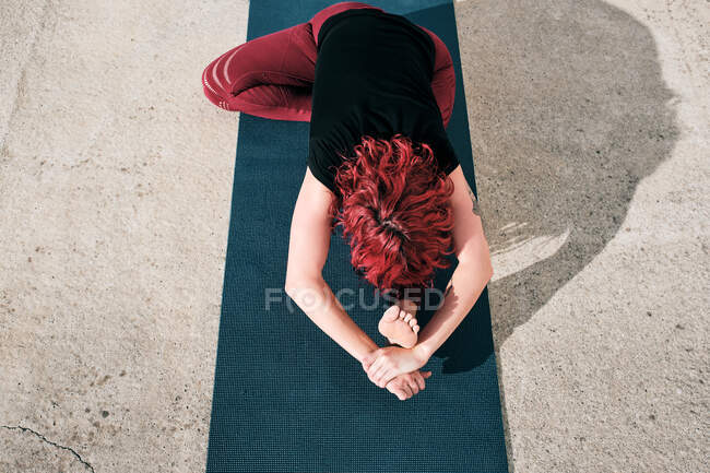 From above top view of unrecognizable flexible barefooted female athlete with red curly hair in activewear sitting practicing yoga — Stock Photo