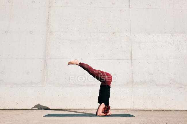 Side view of unrecognizable barefooted female athlete in activewear standing upside down in sirsasana position with legs raised — Stock Photo