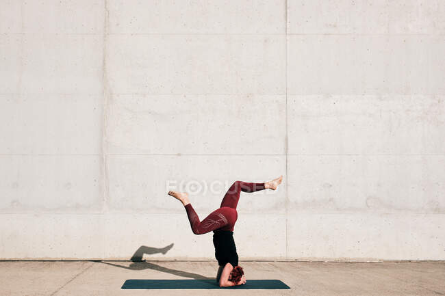 Side view of unrecognizable barefooted female athlete in activewear standing upside down in sirsasana position with legs raised in split — Stock Photo