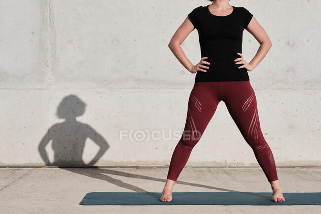 Cropped unrecognizable woman with in sportswear standing on yoga mat against concrete wall after training on the street — Stock Photo