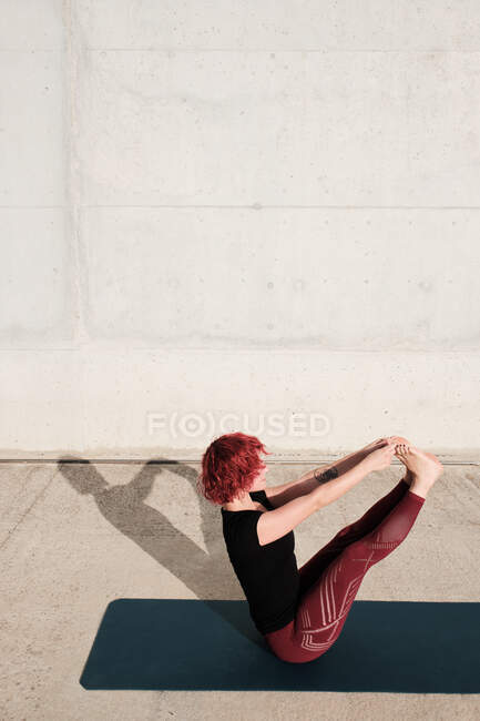 From above side view of unrecognizable barefooted woman with red curly hair in sportswear standing upside down in boat pose — Stock Photo