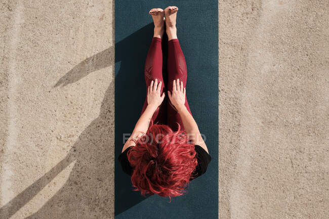 From above top view of anonymous barefooted woman in sportswear sitting resting after yoga exercise on mat on the street — Stock Photo