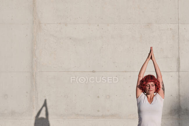 Confident woman with closed eyes athlete in sportswear meditating while standing in vrikshasana position with arms raised and namaste — Stock Photo