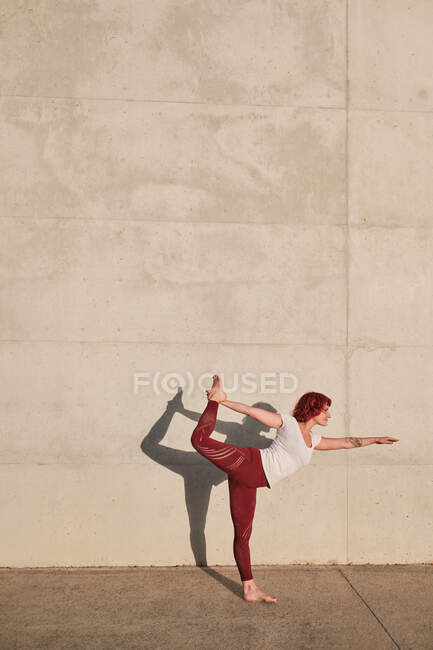 Модний підходить жінка в спортивному одязі робить йогу в лорді танцювальної позі на спортивному килимку під час тренування на самоті на вулиці — стокове фото